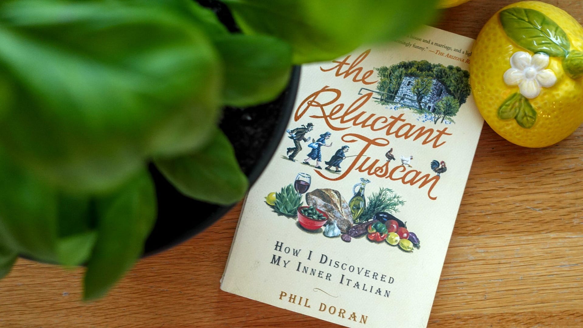 Phil Doran's book The Reluctant Tuscan on a wooden table with basil in the foreground