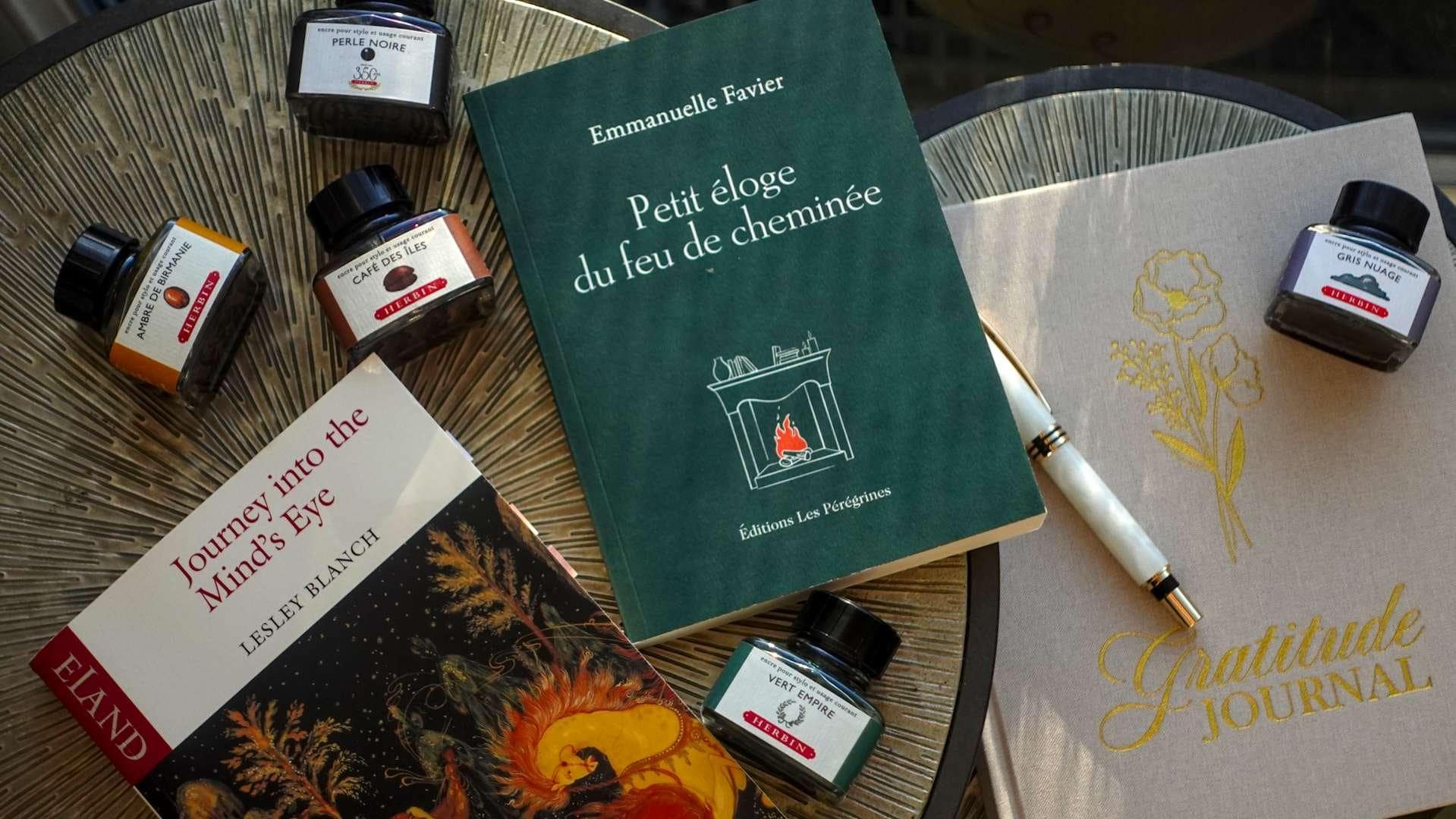 A stack of winter books including Journey into the Mind’s Eye by Lesley Blanch and Petit éloge du feu de cheminée by Emmanuelle Favier on a wooden table