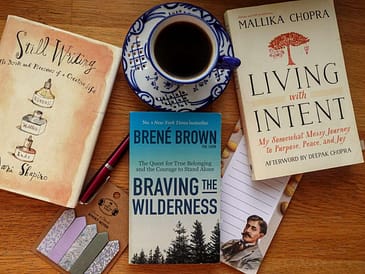 A top-down flat lay of three books: Living with Intent by Mallika Chopra, Braving the Wilderness by Brené Brown, and Still Writing by Dani Shapiro, arranged neatly on a wooden surface.