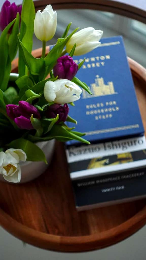 A selective focus portrait of fresh tulips with a blurred background of etiquette books and classic novels, creating a February literary mood board aesthetic for The Ritual of Reading.