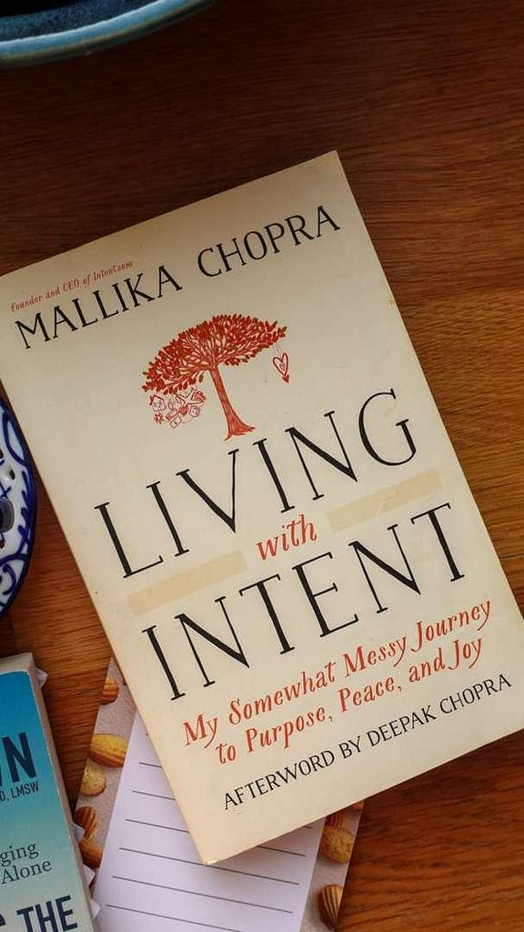 A close-up shot of the book cover for 'Living with Intent' by Mallika Chopra, resting on a neutral background.